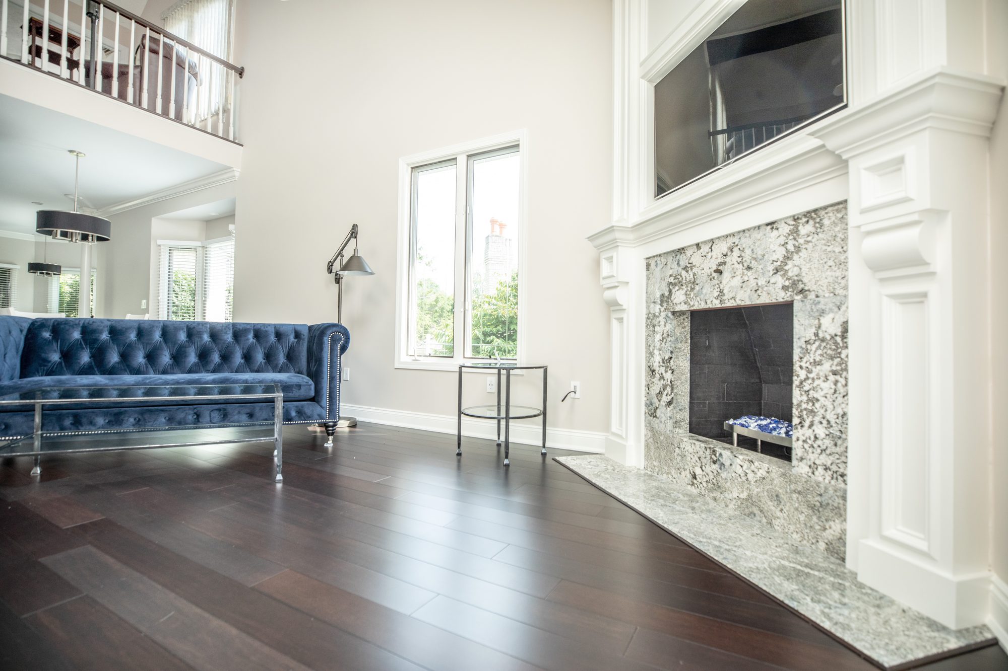 Bright great room remodel with a tufted blue sofa, hardwood floors and a marble fireplace surround
