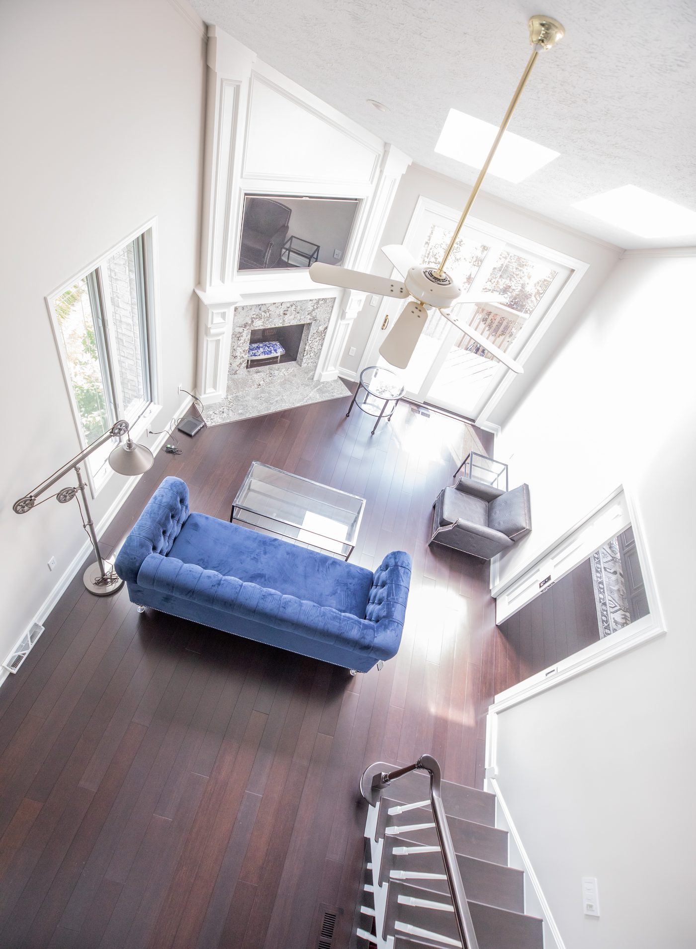 Remodeled great room open to a loft above, with a tufted blue sofa and marble fireplace